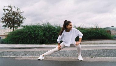 Genç ve mutlu kadın, şehirde sabah egzersizleri sırasında basit ve etkili egzersizler yaparak bacak ve kalça kaslarını pompalamak için derin hamleler yapıyor. Sağlıklı yaşam tarzı, vücudunu formda tutan bir kadın.