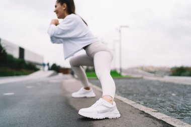Genç ve mutlu kadın, şehirde sabah egzersizleri sırasında basit ve etkili egzersizler yaparak bacak ve kalça kaslarını pompalamak için derin hamleler yapıyor. Sağlıklı yaşam tarzı, vücudunu formda tutan bir kadın.