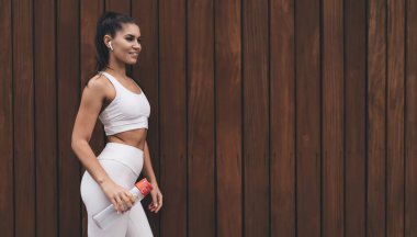 Sağlıklı ve kablosuz kulaklıklı genç bir kadın tanıtım metninin arka planında duruyor. Çekici esmer kadın ince, güzel vücutlu, elinde su şişesi olan, dışarıda duran.