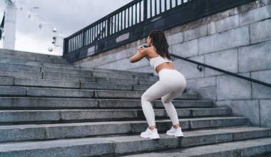 Genç bir kadın, kentteki sabah egzersizleri sırasında kalça kaslarını şişirmek ve formda, basit ve etkili egzersizler yapmak için çömelir. Sağlıklı yaşam tarzı, vücudunu sportif formda tutan bir kadın.