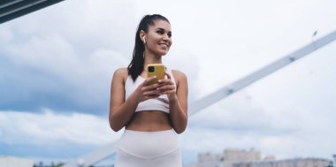 Büyük şehirde kulaklıkların içinde dururken elinde cep telefonu olan çekici bir kadın. Akıllı telefon uygulaması ile kulaklıkla müzik dinleyen genç bir kadın. Sınırsız Mobil internet bağlantısı