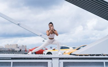 Genç ve mutlu kadın, şehirde sabah egzersizleri sırasında basit ve etkili egzersizler yaparak bacak ve kalça kaslarını pompalamak için derin hamleler yapıyor. Sağlıklı yaşam tarzı, vücudunu formda tutan bir kadın.