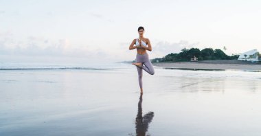 Namaste ağacında duran konsantre kadın meditasyon yapmak ve dengeyi sağlamak için kıyı şeridinde poz veriyor. Yoga eğitimi sırasında hayat enerjisi için dua eden çekici kadın mantraları.