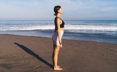 Spor elbiseli beyaz bir kadın, Karayip Denizi yakınlarında meditasyon yapıyor. Eşofmanlı, çekici, aktif bir kız. Sahilde güneş enerjisi alıyor.