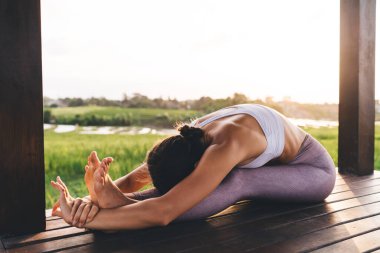 Eşofmanlı kadın vücut kasları için egzersiz yapıyor. Zayıflamak için ilham alıyor. Spor yapan kadın antrenör Endonezya 'da terasta yoga yaparken zevk alıyor.