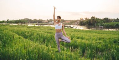 Endonezya 'da yaz tatillerinde yoga yapan mükemmel vücut figürlü zayıf bir kadın. Ağaçta dikilen kadın portresi. Sabahları pirinç tarlalarında duruyor.