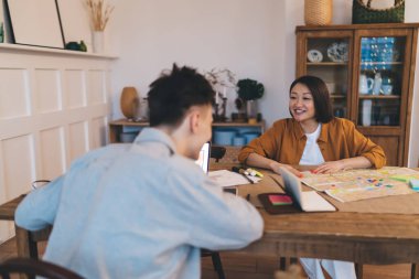 Asyalı kadın ve erkek evde masada konuşuyor. Genç çift gelecekteki hafta sonunu, tatili ya da seyahati planlıyor. Tahta masa, şehir haritası, aletler, ofis malzemeleri ve eşyalar. Geniş bir daire.