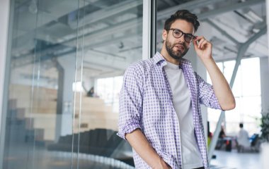 Bin yıllık Kafkasyalı işadamı dikilip kameraya bakıyor. Modern başarılı adam kavramı. Açık uzay ofisinde gözlük takan ve sıradan kıyafetler giyen yakışıklı bir genç.