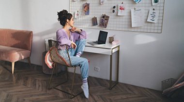 Genç milenyum kadın bilgisayar cihazıyla evde oturup uzaktan kumandayla çalışıyor. Webinar kursuyla çevrimiçi öğrenen kız öğrenci uzaktan çalışmak için taşınabilir netbook kullanıyor