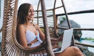 Muhteşem kaygısız genç kadın dizüstü bilgisayarda çalışıyor ve tatillerde deniz manzarasının tadını çıkarıyor. Gülümseyen kadın dijital göçebe Bali 'ye seyahat ederken internette geziniyor