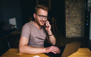 Akıllı Kafkasyalı iş adamı bilgisayarın önünde otururken akıllı telefondan arıyor. Kızıl saçlı erkek serbest internet sitesinde çalışırken cep telefonuyla konuşuyor.