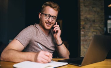 Akıllı Kafkasyalı iş adamı bilgisayarın önünde otururken akıllı telefondan arıyor. Kızıl saçlı erkek serbest internet sitesinde çalışırken cep telefonuyla konuşuyor.