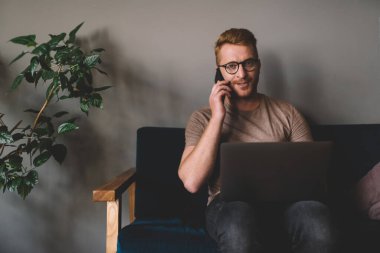Akıllı Kafkasyalı iş adamı bilgisayarın önünde otururken akıllı telefondan arıyor. Kızıl saçlı erkek serbest internet sitesinde çalışırken cep telefonuyla konuşuyor.