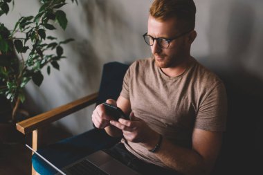 Beyaz saçlı, 30 yaşında, akıllı telefon uygulaması kullanan bir adam içeride dizüstü bilgisayar başında oturuyor. Birlikte çalışma alanında serbest çalışma sırasında cep telefonundan mesaj okuyan genç bir erkek.
