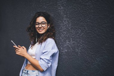 Akıllı telefon cihazıyla gülümseyen bir kadın mobil uygulamadan ses kitabını dinlerken. Kulaklıklı esmer bir kadın cep telefonunda müzik listesinin keyfini çıkarıyor. Reklam için alanı kopyala