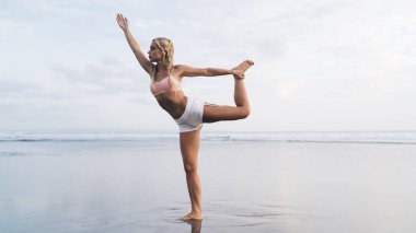 Uzunluk açısı geniş, spor vücutlu beyaz kadın açık havada antrenman yaparken deniz kıyısında esneme egzersizleri yapıyor. Genç bir kadın doğada spor yapıyor ve sağlıklı yaşam tarzının tadını çıkarıyor. Sahilde ısın.