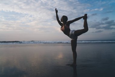 Uzunluk açısı geniş, spor vücutlu beyaz kadın açık havada antrenman yaparken deniz kıyısında esneme egzersizleri yapıyor. Genç bir kadın doğada spor yapıyor ve sağlıklı yaşam tarzının tadını çıkarıyor. Sahilde ısın.