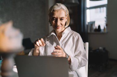Ev sanatları stüdyosunda ışıklandırmayla çalışırken dizüstü bilgisayardan bir şey izleyen kıdemli beyaz iş kadını. Küçük işletmeler ve girişimcilik. Modern başarılı kadın