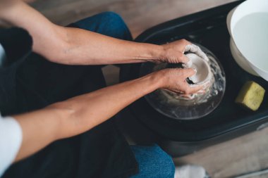 Sanat stüdyosundaki çömlek çarkında kadın toprak kalıbının en üst görüntüsü. Küçük işletmeler ve girişimcilik. Ev hobisi, eğlence ve eğlence. Olgun bir kadının kırpılmış görüntüsü