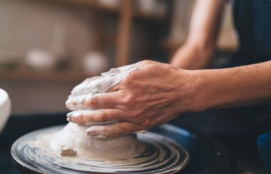 50 yaşındaki kadın heykeltıraşın elleri çömlek çarkında kil çömlek yapıyor. Küçük işletmeler ve girişimcilik. Ev hobisi ve boş zaman. Sanat stüdyosundaki kadının kısmi görüntüsü
