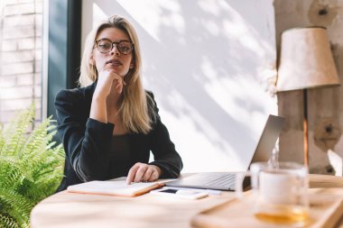 Gündüz vakti kafenin iç kısımlarında kameraya bakan şık ceketli ve optik gözlüklü başarılı kadın yöneticinin portresi modern dizüstü bilgisayar teknolojisiyle iç mekanda poz veren yetenekli bir kadın.