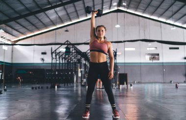 Aktif giyimde olan beyaz kadın spor malzemelerini kilo vermek ve spor hedeflerine ulaşmak için kullanıyor, güçlü atletik kadın antrenmanları ve ağırlık kaldırma antrenmanları sırasında spor salonunda egzersiz yapıyor.