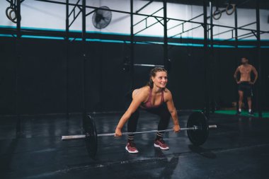 Aktif spor giyimli güçlü beyaz kadın spor salonunda halter kaldırma egzersizi yapıyor. Spor stüdyosunda vücut geliştirme egzersizi yaparken kas geliştirmeye kararlı.