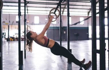 Beyaz kadın sporcunun jimnastik yüzükleriyle barfiks çekişini, spor salonunda vücut egzersizi yapan güçlü formda bir kız - sağlık gücü ve dayanıklılık yarışması