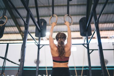 Eşofmanlı sporcu kadın vücut geliştirme egzersizi yapıyor. Jimnastik yüzükleriyle barfiks çekmek için vücut geliştirme egzersizi yapıyor. Vücut ağırlığı ve vücut ağırlığı ile vücut ağırlığı ile vücut geliştirme eğitimine arka plan bakıyor.