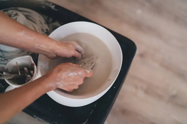 stock image Partial image of female master washing tool in water after molding ceramic pottery at art studio. Concept of small business and entrepreneurship. Home hobby, entertainment and leisure. Top view