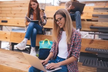 Üniversite kampüsünde dizüstü bilgisayar ve kitaplarla oturan bir grup öğrenci. Üç arkadaş okul dersleri için ev ödevi öğreniyor ve hazırlıyor. Web 'de kadın klavye isteği