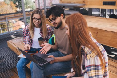 Bir grup öğrenci, kampüste dizüstü bilgisayarlarıyla otururken üniversite projesinde beyin fırtınası yapıyorlar. Üç arkadaş birlikte öğreniyor ve netbook 'ta online bilgileri tartışıyorlar.