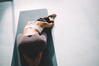 Childs 'ta yoga yapan kadın geniş bir evde poz veriyor. Uyum ve akıl sağlığı kavramı. Genç ve güzel esmer atletik kız spor giysisi giyiyor ve spor minderinde çıplak ayakla dolaşıyor.