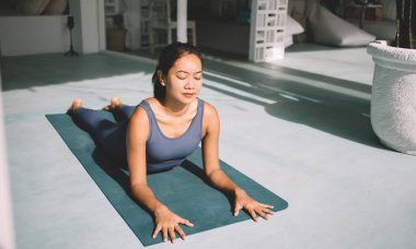 Kobra esneme pozisyonunda yoga yapan Asyalı bir kız. Sağlıklı yaşam tarzı kavramı. Genç, çekici, esmer, gözleri kapalı, spor giyimli, spor ayakkabılı ve spor minderinde çıplak ayaklı bir kadın.
