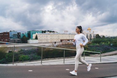 Beyaz spor giysili atkuyruklu, yaz günü antrenman yaparken kaldırım köprüsünde koşan atletlerin yan görüntüsü.