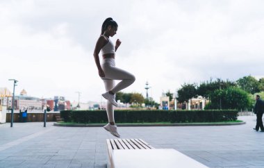 Şehir meydanındaki spor salonunda egzersiz yaparken spor kıyafetleri içinde uzun siyah saçlı aktif formda genç bayan sporcuların yan görüntüsü.