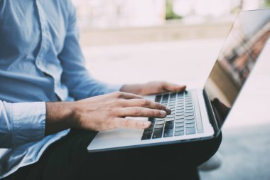 İnternet sörfü yaparken klavyede yazan yüzü olmayan, beyaz gömlekli ve siyah pantolonlu bir adamın yan görüntüsü.