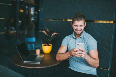 Açık kafede saksıda bitki ve laptopla otururken cep telefonuyla mesajlaşan olumlu erkek mesajları.