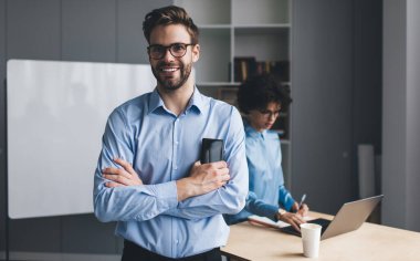 Akıllı telefonlu bir iş adamı kameraya bakarken bayan meslektaşı dizüstü bilgisayarda yazı yazıyor. Modern başarılı insanlar. Genç Kafkas milenyum insanları ofiste.