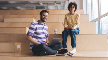 Not defteri olan bir iş kadını ve kameraya bakan bir iş adamı. İş birliği ve takım çalışması. Çalışma odasındaki ahşap banklarda oturan Kafkasyalı meslektaşlar. Modern başarılı insanlar