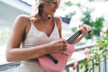 Otel balkonunda ukulele çalan beyaz bir kadının kısmi görüntüsü. Eğlence, eğlence ve hobi anlayışı. Tatil ve hafta sonu fikri. Dövmeli, gülümseyen kız. Bali adası