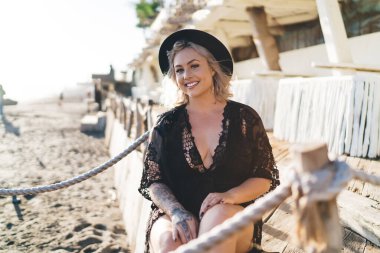 20 'li yaşlardaki mutlu beyaz kadın, turistik gezi sırasında kumsalda dinlenirken kameraya gülümsüyor, siyah bikini mayo giymiş neşeli bayan yüzücü Endonezya' da güneşlenirken eğleniyor.