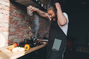 Evde taze sebzelerle tezgahta dururken önlüklü komik, genç ve sakallı aşçı bağırıyor ve tencereye farfalle makarna döküyor.