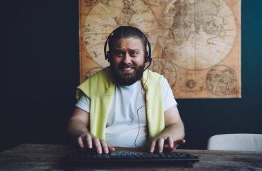 Evde video oyunu oynarken, kulaklık takan ve klavyede daktilo yazan konsantre olmuş, sakallı genç erkek oyuncu.