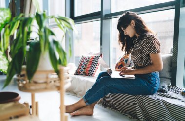 Genç ve çekici bir kadın dizlerinin üstünde dizlerinin üzerinde bilgisayar başında oturmuş Webinar 'la internetten ders çalışıyor. Uzaktan çalışırken ve netbook ile çevrimiçi alışveriş yaparken güzel kadın serbest yazar ağı tarıyor