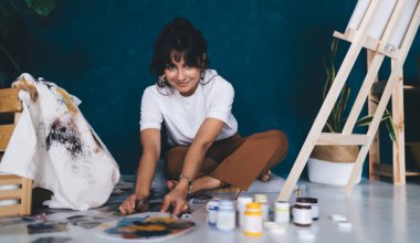 Çekici genç bayan ressam resim çiziyor ve hobisinin rahatlatıcı sürecinden zevk alıyor. Yaratıcı ve yetenekli esmer kadın sehpada resim yaratıyor. Petrolle çizim yapmayı öğrenmek