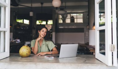 Genç Mutlu Kadın, birlikte çalışan dizüstü bilgisayarında çalışırken eğleniyor. Gülümseyen, kaygısız, serbest çalışan kadın, açık bir ağ kitabının önünde oturuyor. Öğrenci Webinar 'da uzaktan öğreniyor