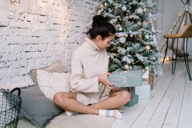 Genç Asyalı kadın evdeki Noel ağacının yanında kürklü halıda otururken hediye kutularına bakıyor. Noel ve yeni yıl zamanı. Milenyum kuşağının esmer kızı. Ev hayatı işte. Geniş bir daire