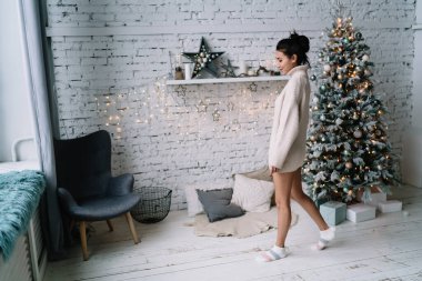 Genç gülümseyen Asyalı kadın elinde hediye kutularıyla Noel ağacının yanına gidiyor. Noel ve yeni yıl zamanı. Milenyum kuşağının çekici esmer kızı. Ev hayatı işte. Geniş daire