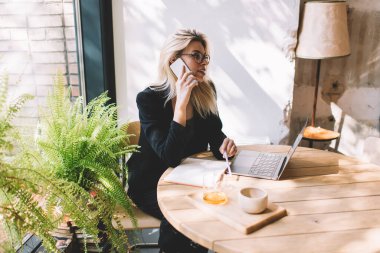 Gözlüklü beyaz bir kadın çalışma alanındaki uzak iş sırasında dizüstü bilgisayarın güncellemesini tartışmak için servis yapıyor. Netbook 'u olan bin yıllık kadın konuşmak için cep telefonu uygulaması üzerinden arıyor.